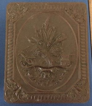 A brown photo case with an intricate design, inset into the material, a frame and detailed ornamentation at the corners, and a 