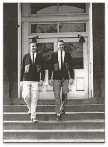 Two young men wearing letterman sweaters, with a W on one side of the buttons and a V on the other. They walk down concrete steps and smile.