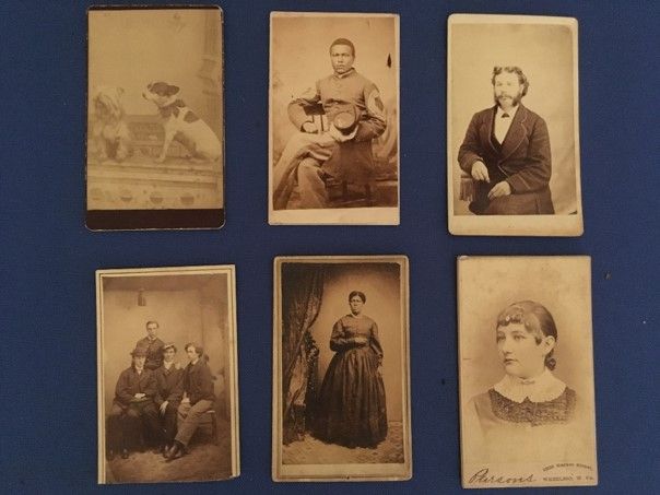 A selection of six CDV images against a dark blue mounting board: two gods, a black man sitting in a chair, a white man sitting, a group of four people, a black woman in a long dress, and a young white woman from the shoulders up.