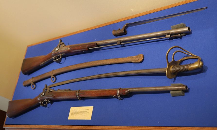 Two muskets and a cavalry sabre displayed against a blue background