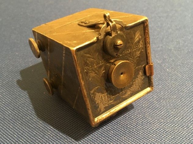 A large brass cube with two circular additions on the front.