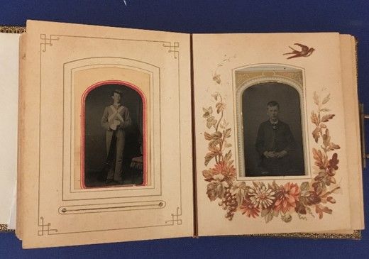 An open photo book showing two tintype images, one framed on each page. The one on the left shows a man in a uniform, framed by concentric lines. The one on the left shows a man, and the photo is framed by several flowers. 