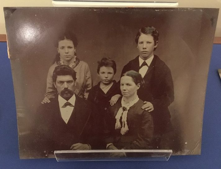 A tintype portrait of a family, two parents, an older boy, a girl, and a young boy. The parents sit in front while the children stand behind them.