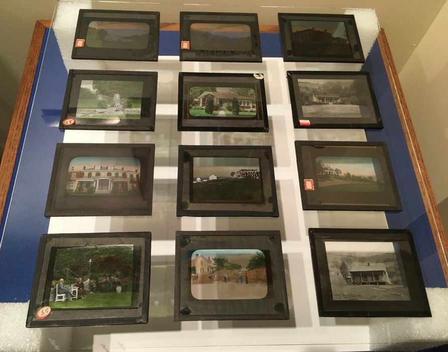 A selection of twelve magic lantern slides displayed on a table. they show landscapes, houses, and various outdoor vistas. some are in color and others are black and white.