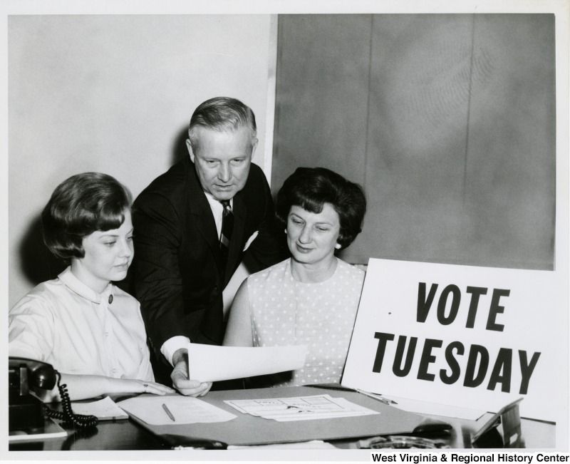 Black-and-white photograph of Arch Moore with Shelley Moore and a girl sitting next to a sign that says "Vote Tuesday"