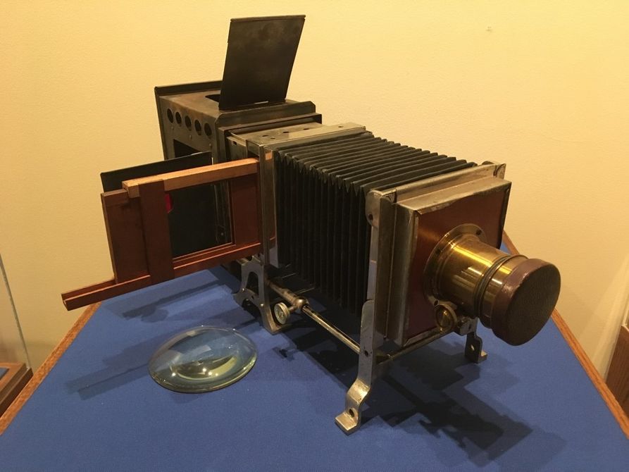 A magic lantern slide projector, a long black box with a lens at the front and a slide holder on the right side. 