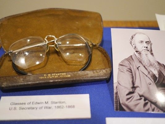 Pair of glasses in a brown lined case next to a photo of a man with a beard.