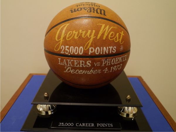 a basketball commemorating Jerry West scoring 25,000 points. It has his name printed on it, as well as the words "25,000 points" and "Lakers vs. Phoenix, 1973." it is on a black pedestal that reads "25,000 career points"