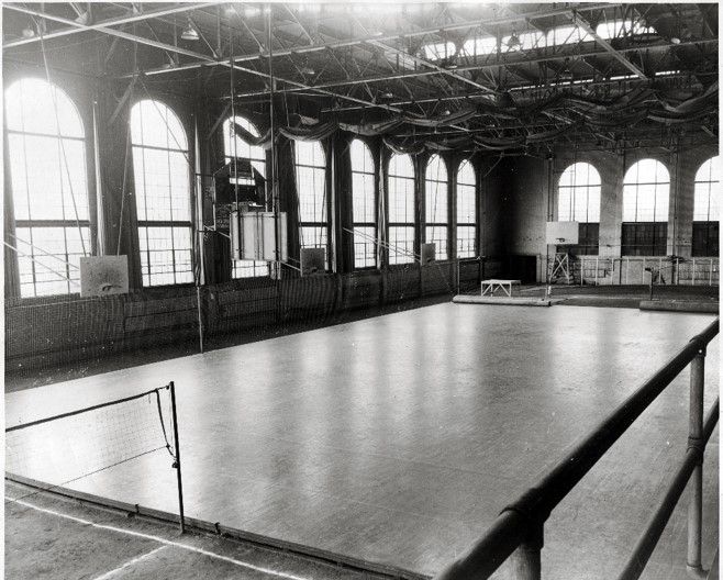 The inside of a large, airy room. The ceiling rafters are high and there are several arched windows letting in the sun. 