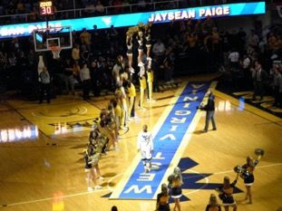 On-court image of modern version of the same ceremony, a blue carpet with gold letters spelling "West Virginia"