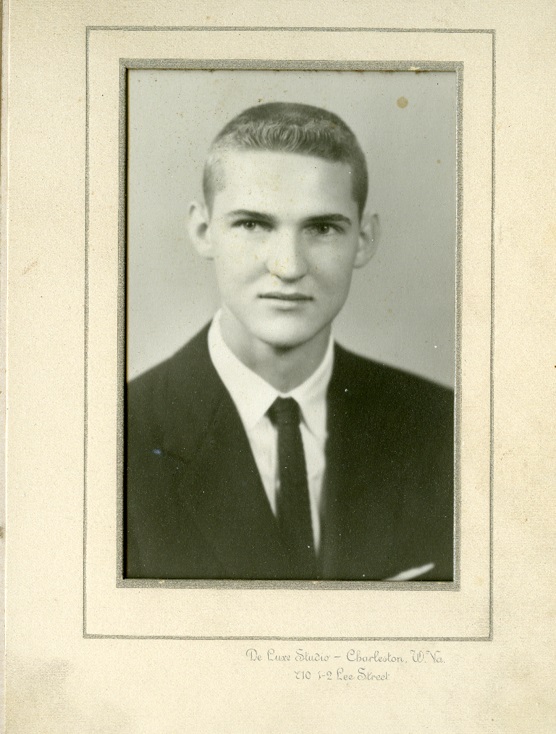 A young Jerry West wearing a suit and tie looks thoughtfully past the camera. He has short hair, a square face, and a serious expression