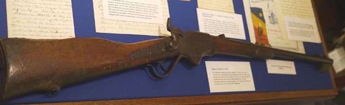 Spencer repeating rifle displayed against a blue background surrounded by documents 