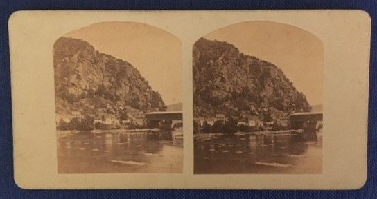Stereograph slide of the edge of a large hill covered in trees, right on the edge of a body of water