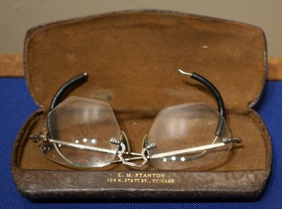 A pair of hexagonal shaped spectacles in a brown leather case with a lighter brown lining. they are resting upside down with the legs pointing toward the sky