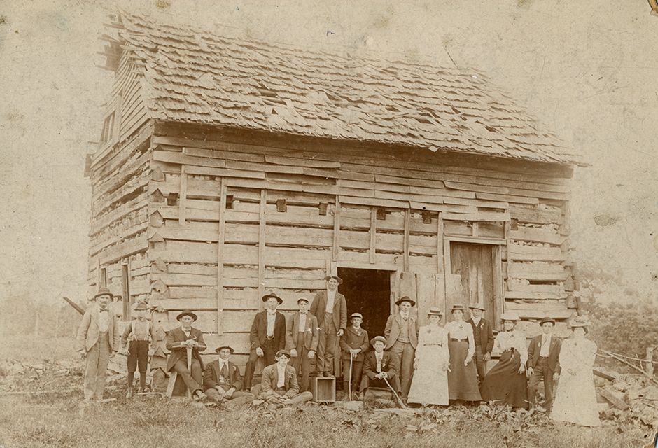 Group of people in front of log cabin.