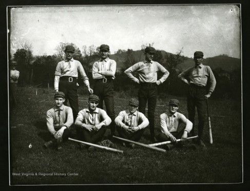 Eight young men in baseball uniforms pose outside with their bats