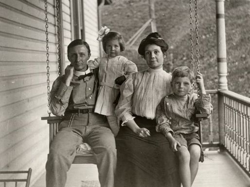 A black-and-white photograph of a family of four on a porch swing
