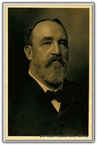 a middle-aged man with a medium length beard, smoothed hair, and a jacket over a white shirt with a bowtie. his expression is neutral and serious