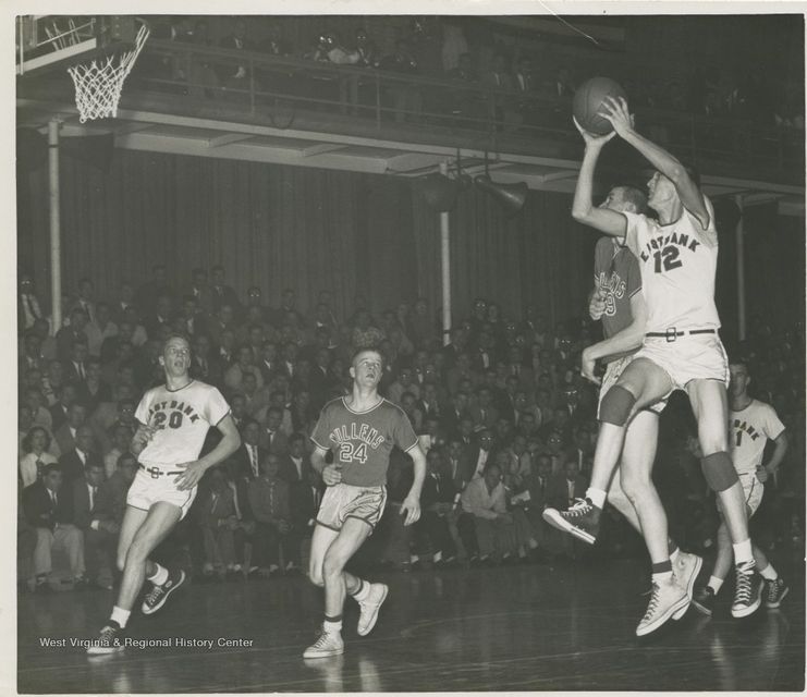 Photograph of Jerry West shooting a basketball with four other players near him. 