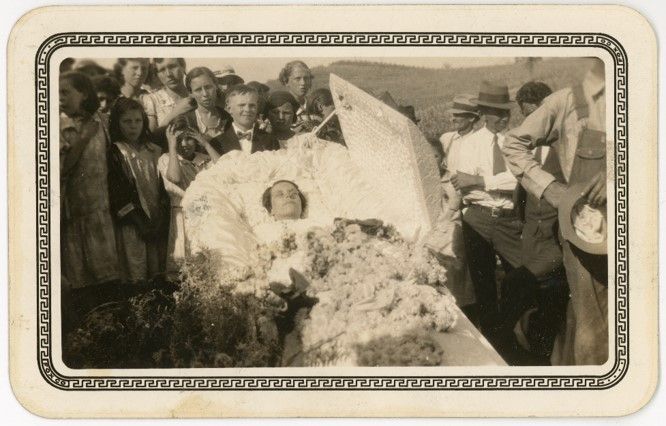 A coffin holding a young person, surrounded by flowers and people