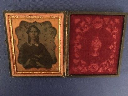 A tintype portrait of a young woman next to a red, detailed photo case. 