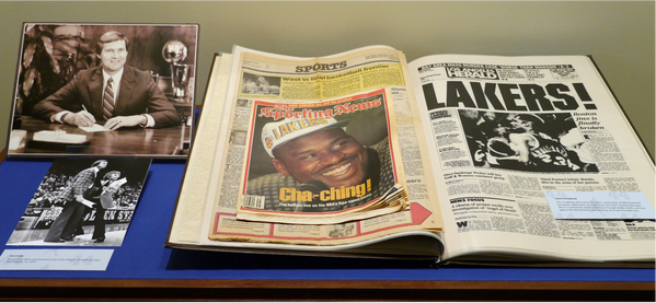 a display of two photos of Jerry as a coach, to the right is an open book with news paper clippings and advertisements concerning the LA Lakers