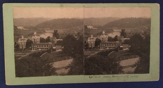 Stereograph of brick buildings nestled in trees and hills