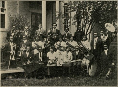 A large group of young black men and women, carrying various instruments