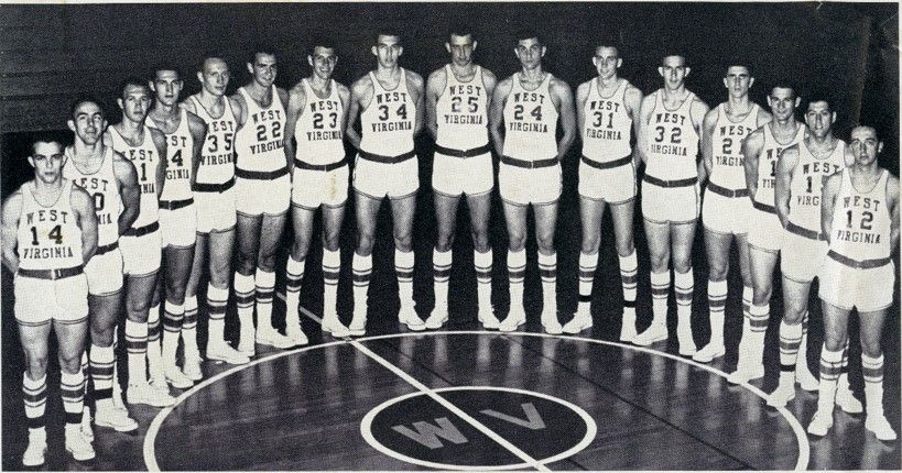 A basketball team in white uniforms stand in a semi-circle at center court