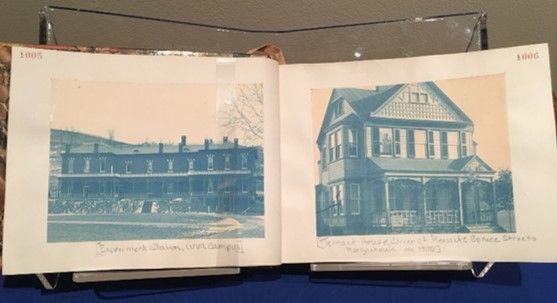 A photo album open to two cyanotypes: the left a long two-story building and the right a large house with a porch.