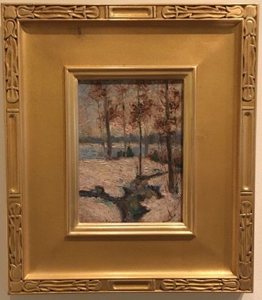 A portrait, painted-over photo photo of a narrow path running through snow-covered ground. Three thin trees with brownish orange leave stand. In the distance, water and hills. The sky is a pale blue. It is a small rectangle in a large gold frame. 