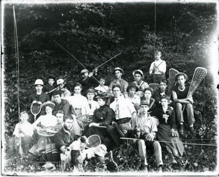 A large group of young men and women sit outside holding various sports equipment