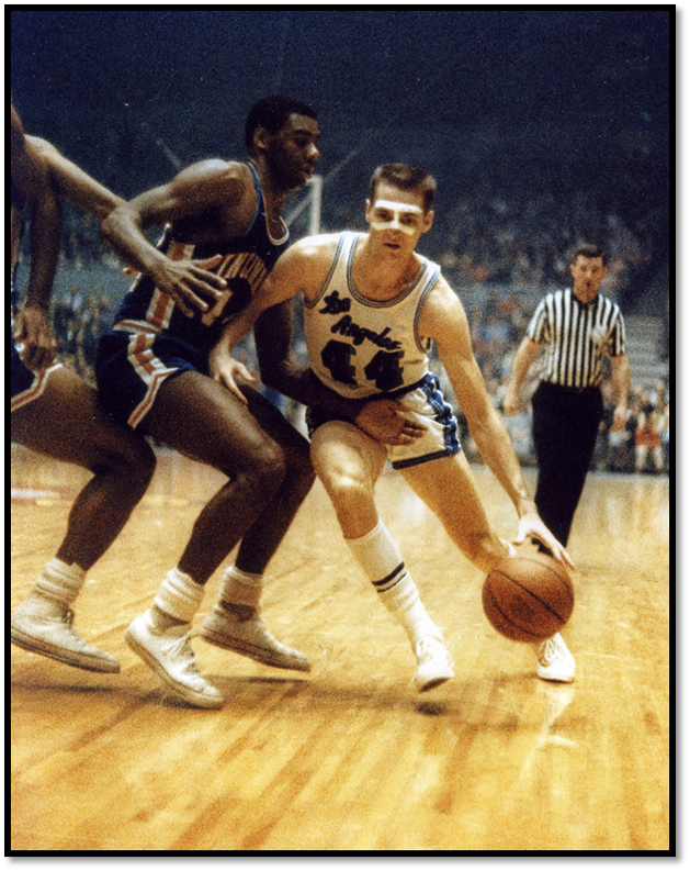 Two basketball players on the court in mid-motion. The player on the left is black and wearing a dark blue uniform, the other player's elbow is pressed against his chest to block him. This is Oscar Robertson. The other player is jerry west, who dribbles. 