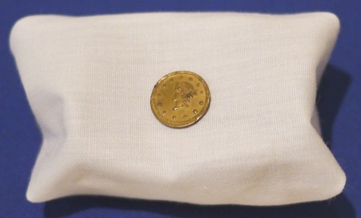 A Confederacy coin on a small cloth stand with a blue background. 