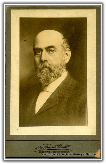 a balding man with a medium length gray beard and a stern expression.